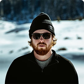 Петя Демин с рыжей бородой в темных очках на фоне снежных холмов